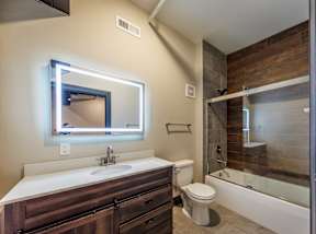 A bathroom with a white sink and a mirror with a light around it.