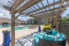 A wooden pergola over a patio with a wicker chair and a blue vase.