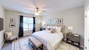 A bedroom with a bed, nightstand, chair, and pictures on the wall.