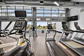 A treadmill with a screen and a handlebar is in a gym.