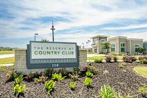 A sign for The Reserve at Country Club Apartment Homes stands in front of a building.