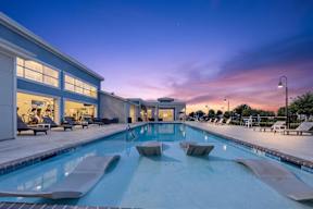 A large indoor swimming pool with lounge chairs and a building with large windows in the background.