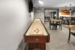 A shiny wooden pool table with red balls is in the middle of a room with a TV and a bar.