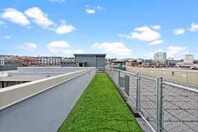 A rooftop with a metal fence and a green lawn.