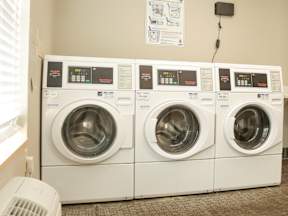 Three identical front loading washing machines are lined up in a laundromat.