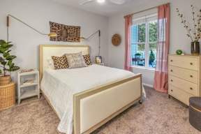 A bedroom with a large bed, a nightstand, and a window with pink curtains.