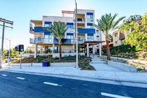 A modern apartment building with blue and white balconies and a street in front.