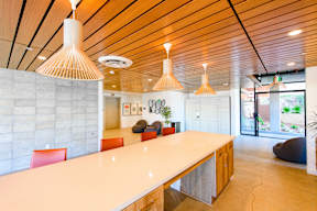 A long white table with red chairs and a white ceiling with hanging lights.