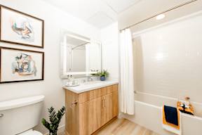 A bathroom with a white tub, a wooden cabinet, and a mirror.