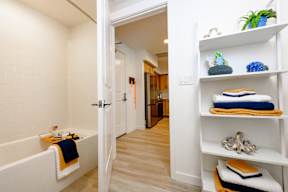 A bathroom with a white tub and a white shelf with towels and a plant.