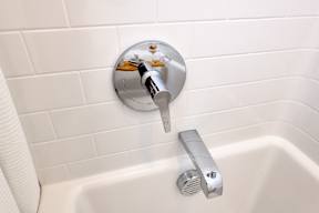 A silver faucet is mounted on a white tiled wall.