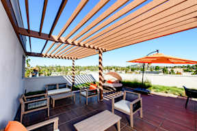 A wooden patio with a bench, table and umbrella.