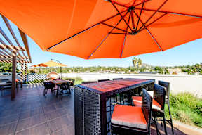 A table with chairs and an orange umbrella on a patio.