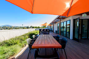 A long wooden table is surrounded by chairs under an orange canopy.