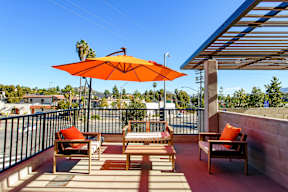 A patio with a table and chairs under an orange umbrella.