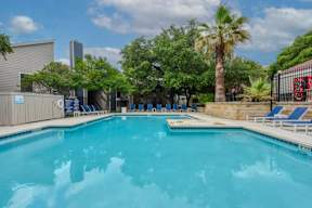 A large swimming pool surrounded by trees and lounge chairs.