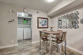 A laundry room with a washer and dryer, a dining table with chairs, and a mirror with a frame.