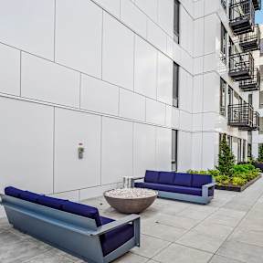 A modern outdoor seating area with a white wall, a blue bench, and a fire hydrant.
