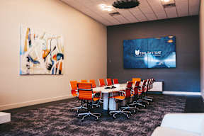 A conference room with a large screen and orange chairs.