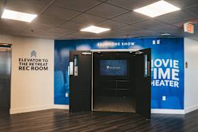 A room with a sign that says "Elevator to the Retreat" and "Enjoy the Show" with a screen and a door.