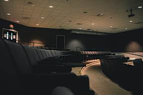 A dark auditorium with rows of seats and a projector screen.