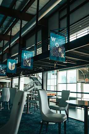 A sign that says "Work" is hanging from the ceiling in a room with tables and chairs.