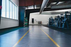 A gym with blue flooring and yellow lines, a row of blue chairs, and a weight rack.