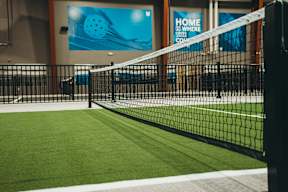 A tennis court with a net and a sign that says "Home is where the game is".