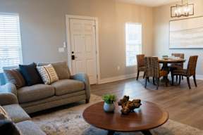 A living room with a grey couch, a brown coffee table, and a dining table with chairs.