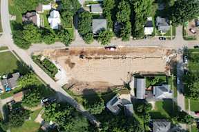 A construction site is surrounded by houses and trees.