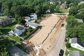 A construction site is surrounded by houses and trees.