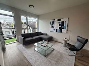 A modern living room with a grey sofa, a glass coffee table, and a black chair.