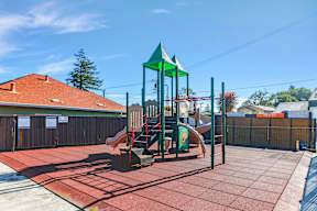 A playground with a green slide and red roofed building in the background.
