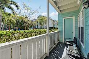 A balcony with a table and chairs overlooks a green yard.