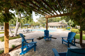 a covered patio with blue chairs near a swimming pool