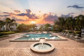 a pool with a fountain and two pools and chairs at sunset