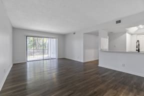 an empty living room with a sliding glass door and a kitchen in the background
