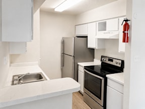 A kitchen with white appliances and a red fire extinguisher on the wall located at Canfield Lakes Apartments in Houston TX