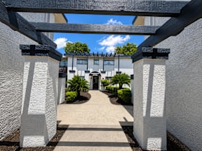 A white archway leads to a building with a black roof leading to the apartment located at the pointe apartments in Pasadena, Tx