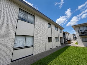 A row of white brick apartment buildings with green grass in front located at the pointe apartments in Pasadena, Tx