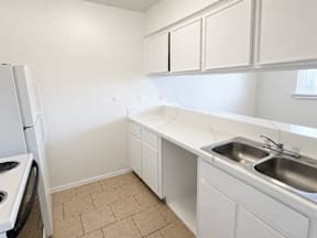 A kitchen with white cabinets and a tiled floor located at the pointe apartments in Pasadena, Tx