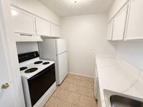 A kitchen with a stove, refrigerator, and sink located at the pointe apartments in Pasadena, Tx