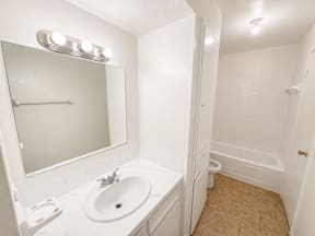 A white bathroom with a sink, mirror and tub located at the pointe apartments in Pasadena, Tx