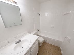 A white bathroom with a sink, toilet and bathtub located at the pointe apartments in Pasadena, Tx