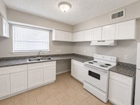 A kitchen with white appliances, cabinets, stove and drawers located at the pointe apartments in Pasadena, Tx