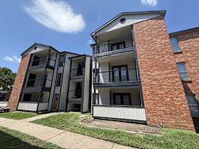 A red brick building with a white balcony located at Canfield Lakes Apartments in Houston TX