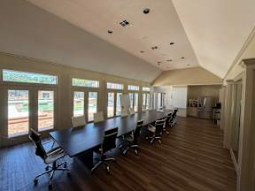 A conference room with a long table and chairs, large windows, and a view of a garden outside located at Canfield Lakes Apartments in Houston TX