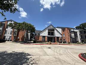 A parking lot in front of a building with a red brick facade located at Canfield Lakes Apartments in Houston TX