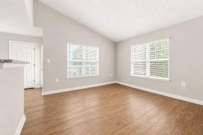 A room with wooden floors and two windows with blinds.