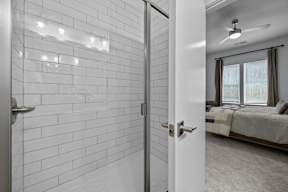 A white tiled bathroom with a white door and a bedroom with a bed and a ceiling fan.at Address East End, Raleigh North Carolina